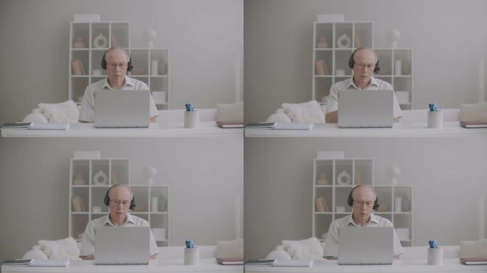 老年男老师正在网上授课，呆在家里，使用带互联网连接的笔记本电脑和耳机