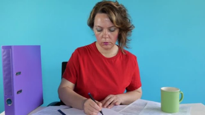 一位穿着红色t恤的四十岁妇女坐在桌子旁时在纸上写了些东西。成年妇女的肖像