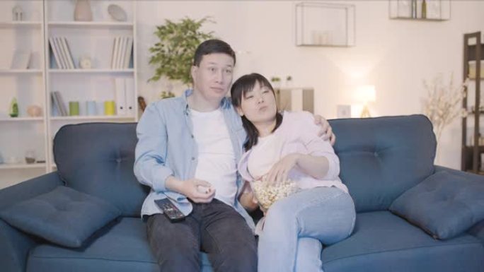 幸福的亚洲夫妇坐在沙发上一起看电视回家，恋爱关系