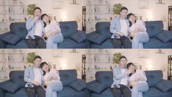 幸福的亚洲夫妇坐在沙发上一起看电视回家，恋爱关系