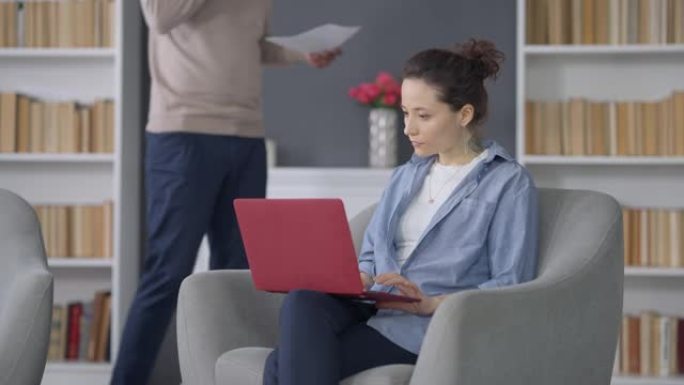集中年轻漂亮的女人在笔记本电脑键盘上打字，男人在后台走路，文件在电话上聊天。被非洲裔美国丈夫分心的受