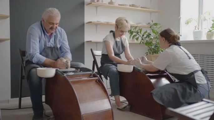 一位女陶工的车轮雕刻老师解释了如何工作，并教一位老年妇女用粘土工作并制作杯子和水罐。养老金领取者大师