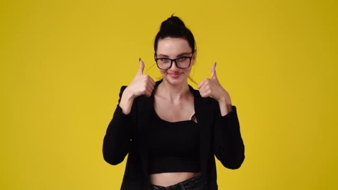 4k慢动作视频，一个女孩指着相机，在黄色背景上竖起大拇指。