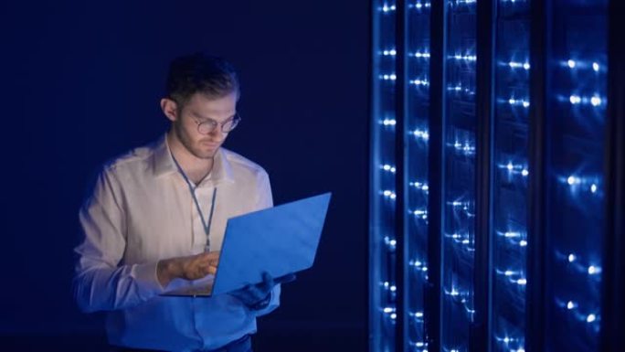男性网络工程师用笔记本电脑站在服务器机房进行系统检查。在数据中心，男性服务器专家检查机架式服务器计算
