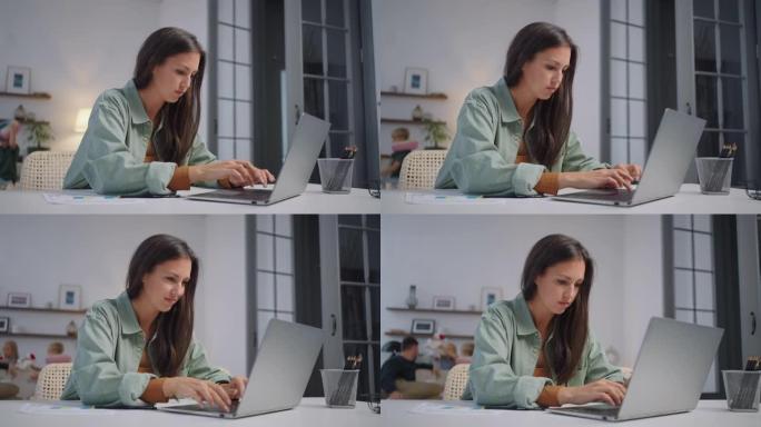 一名女商人在笔记本电脑上远程工作，并在家庭在后台唱歌时在网络摄像头上显示图表。忙碌的女商人。小型企业