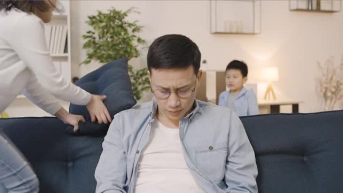 苦恼的亚洲父亲在家中使用笔记本电脑，顽皮的孩子四处游荡