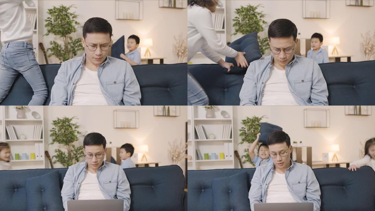 苦恼的亚洲父亲在家中使用笔记本电脑，顽皮的孩子四处游荡
