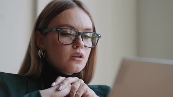 迷人的成年女性的肖像，戴着笔记本电脑的眼镜，看着显示器，特写镜头