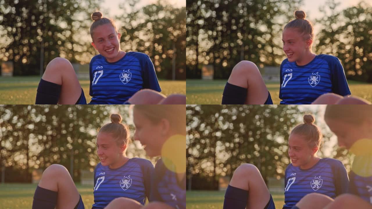 SLO MO年轻的女足球运动员坐在运动场上与队友交谈