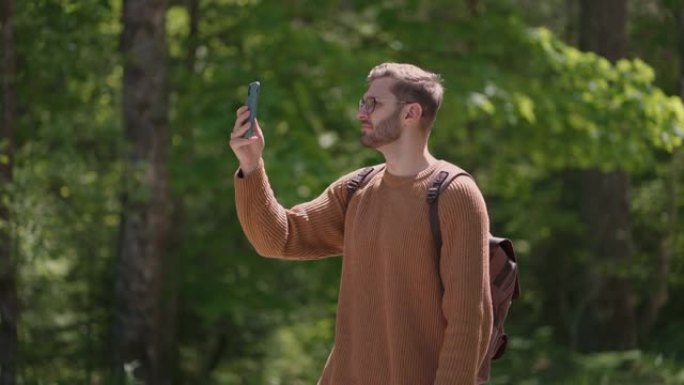 男子徒步旅行者在森林里享受周末时使用智能手机。手机上迷人的男人背包客规划森林旅行路线的低角度视图