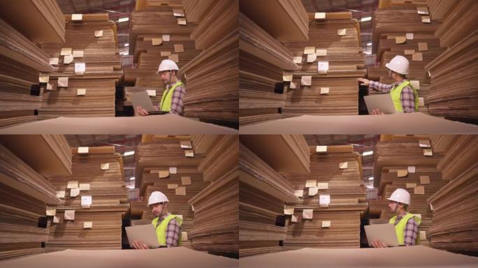 聪明的亚洲工程师穿着安全反光背心和硬头盔做库存勾检查，并在工厂仓库背景中清点纸板库存产品。纸厂管理理