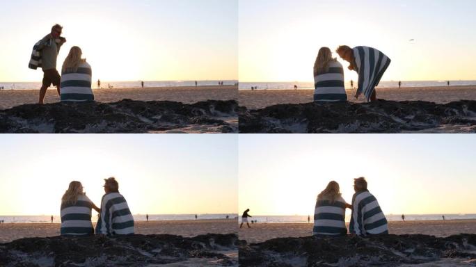 日落时分，情侣在安静的海滩上的毛巾下放松