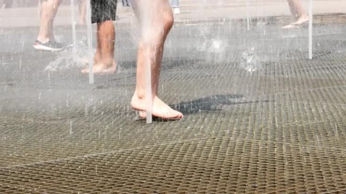 一股水流在喷泉的一根柱子上升起，光着脚的人在水中沐浴。夏天的乐趣。在闷热中振作起来