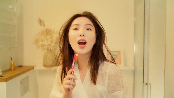 感觉棒极了。亚洲女性享受早上的浴室活动，在镜子前玩得开心。对着牙刷唱歌