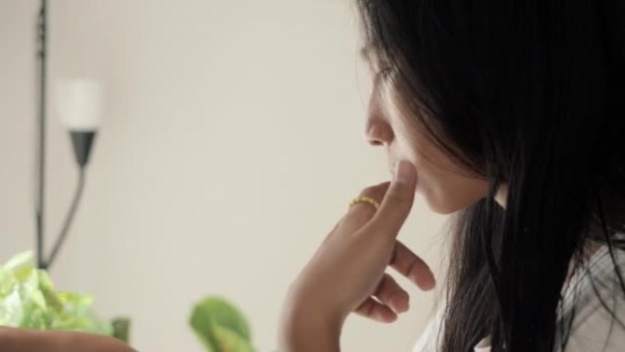 周末，亚洲女孩在家里的窗户附近吃完零食后，用智能手机看电影或病毒视频，舔手指。
