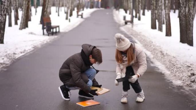 可爱的少年男孩帮助女孩在公园巷收集倒下的书。放学后的冬天在户外拍摄的白人青少年夫妇的照片。