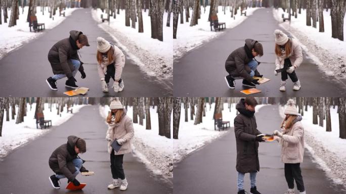 可爱的少年男孩帮助女孩在公园巷收集倒下的书。放学后的冬天在户外拍摄的白人青少年夫妇的照片。