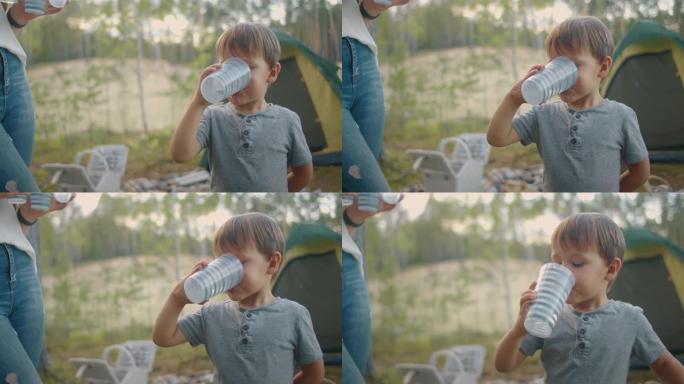 夏天，小男孩在森林的帐篷营地用玻璃喝水，家人在大自然中休息