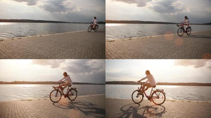 穿着白色衣服的开朗女孩在阳光明媚的日子里在湖边骑自行车，抬起腿