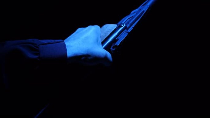 在蓝色照明的黑暗中，一支枪在一个准备开火的人手中