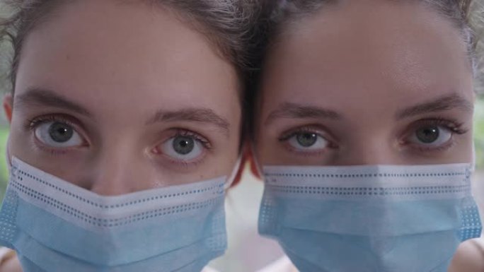 冠状病毒面具的同卵双胞胎姐妹的特写眼睛看着相机，表情严肃。身材苗条的年轻美丽的白人妇女新型冠状病毒肺