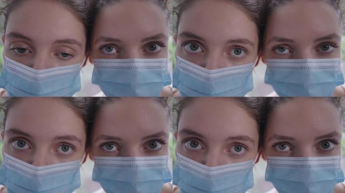 冠状病毒面具的同卵双胞胎姐妹的特写眼睛看着相机，表情严肃。身材苗条的年轻美丽的白人妇女新型冠状病毒肺