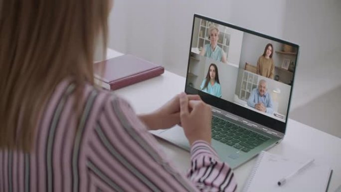 女性员工在网上简报中与不同种族的同事进行视频通话的后视图，女性员工在家里的现代笔记本电脑上与同事举行