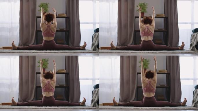 瑜伽女正在做分开和伸展双手，在客厅的女性身体的后视图，瑜伽和体操练习