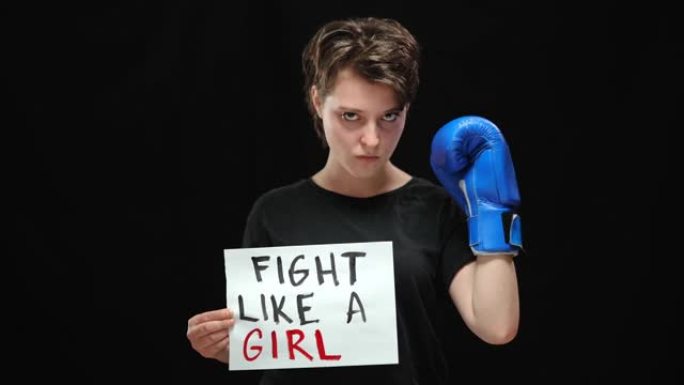 自信的严肃的女人在拳击手套中像女孩一样看着相机。自信的高加索女性活动家在黑色背景下为争取平等人权而战