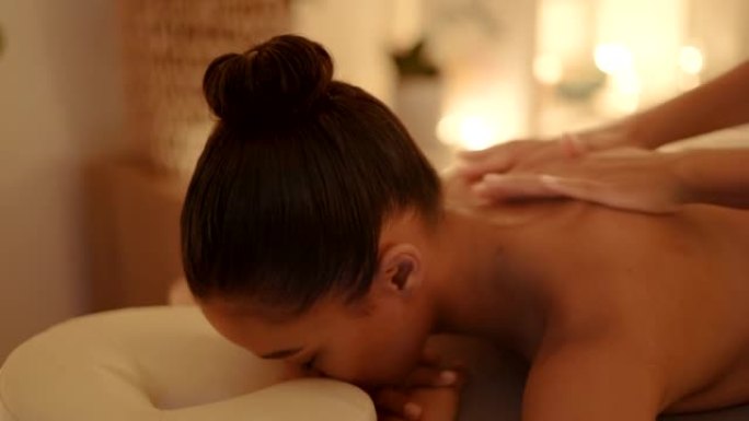 年轻女子在水疗中心做背部按摩。女性在桌子上放松，闭着眼睛，一边接受温和的身体治疗
