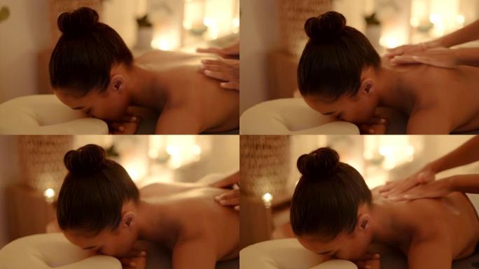 年轻女子在水疗中心做背部按摩。女性在桌子上放松，闭着眼睛，一边接受温和的身体治疗