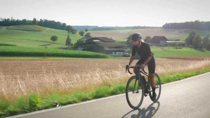 自行车和铁人三项概念。女人骑自行车，日落时带着太阳透镜耀斑在乡下爬坡。适合运动型女自行车手在激烈的自