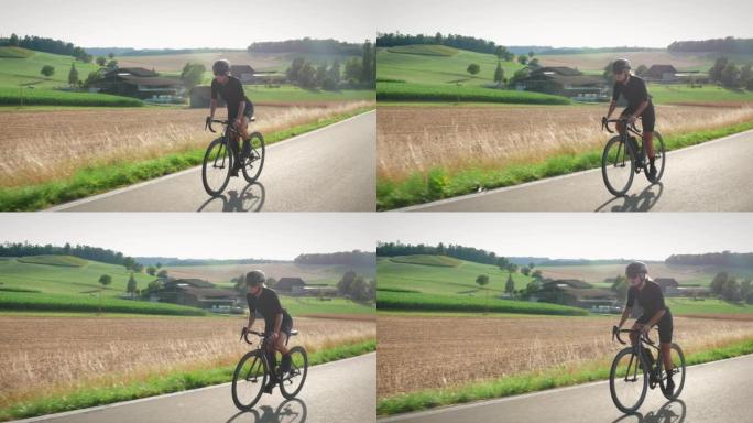 自行车和铁人三项概念。女人骑自行车，日落时带着太阳透镜耀斑在乡下爬坡。适合运动型女自行车手在激烈的自