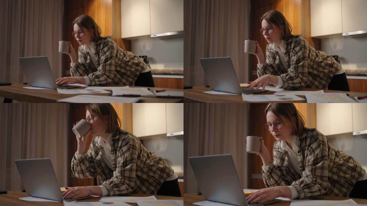 美丽的年轻女子坐在客厅喝咖啡时在笔记本电脑上工作。在笔记本电脑上工作的快乐休闲美女。在家使用笔记本电