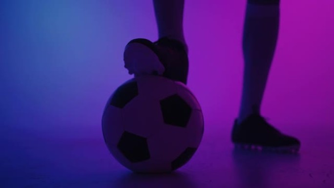 在演播室蓝红色霓虹灯下慢动作站立在球上的一名职业黑人足球运动员的脚的特写镜头。巴西足球运动员脚踩球摆
