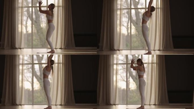 一位穿着白色运动服的年轻女子正伸展着一个大大厅，大厅里有大窗户，以慢动作的方式，阳光透过窗户。健康的