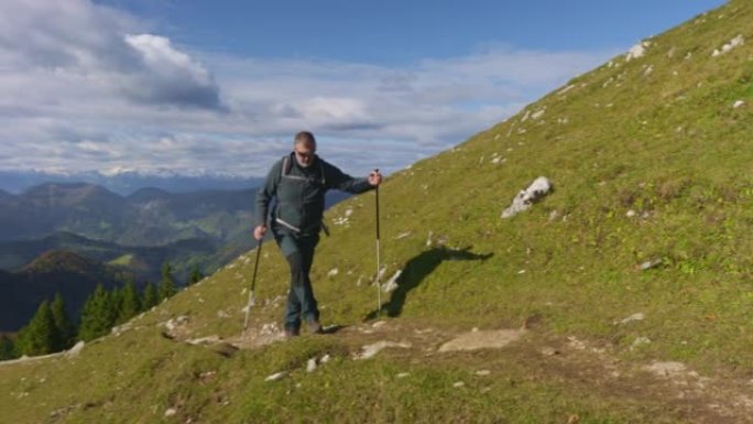 高级男性徒步旅行者在阳光下的风景优美的小径上爬山