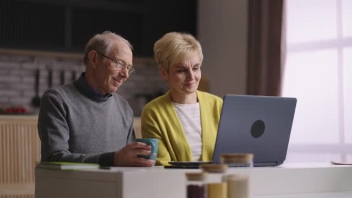 老年已婚夫妇正在与家人和朋友通过视频通话聊天，向笔记本电脑的网络摄像头挥手