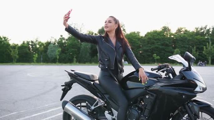 美丽快乐微笑的年轻时尚女性骑自行车的黑色衣服坐在豪华摩托车上自拍