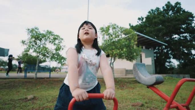 亚洲小女孩在户外操场玩跷跷板很开心