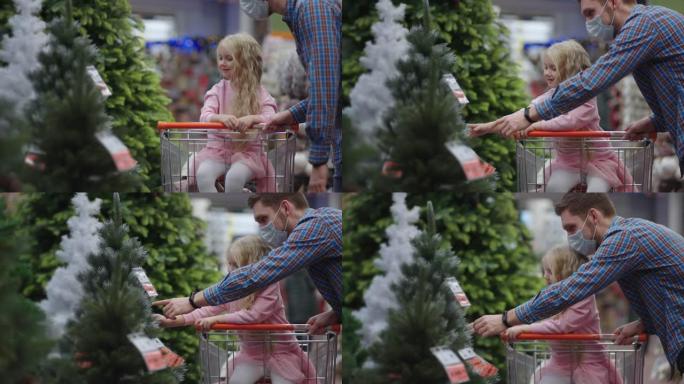 爸爸和孩子选择商店货架上的圣诞玩具。购物车里的父亲和小女儿选择圣诞装饰品。购物中心的慢动作