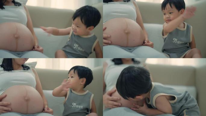 蹒跚学步的男孩在卧室里亲吻他怀孕的母亲的肚子。