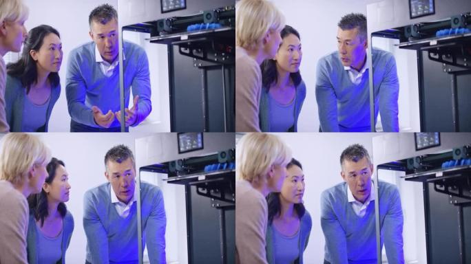 一位亚洲男工程师和他的两位女同事在3D打印机中研究模型的构建并讨论了进展