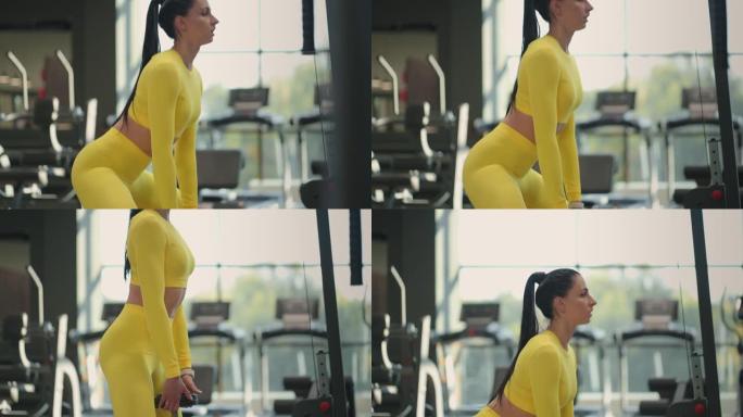 年轻的西班牙裔黑发女子穿着黄色运动服蹲在健身房里拿着哑铃