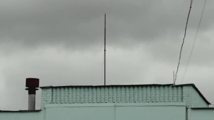 强风将房屋屋顶上的电线和天线震动在云雾笼罩的灰色天空的背景下。被闪电击中的危险，阴云密布