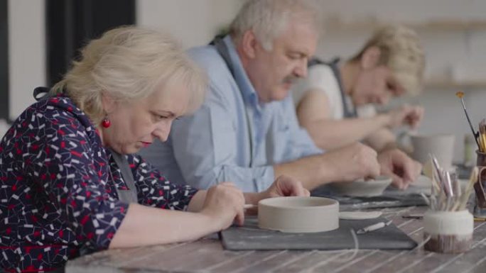 一群在陶器大师班上的老人一起在陶杯上雕刻和切割绘画，以制造陶瓷餐具