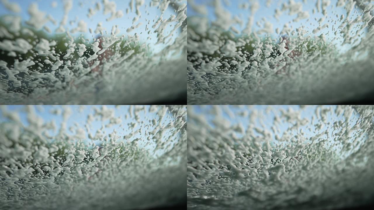 挡风玻璃用白色洗车洗发水在阳光下慢动作喷洒。户外洗车服务的不知名员工洗车。汽车维修概念。