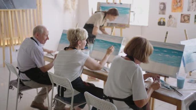 慢动作老人参加绘画课程。老师帮助参加绘画课程的养老金领取者绘画。一群退休的朋友在绘画课上