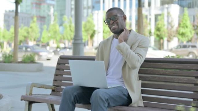 坐在户外长凳上时使用笔记本电脑颈部疼痛的非洲男子坐在户外长凳上时使用笔记本电脑颈部疼痛的非洲裔美国人
