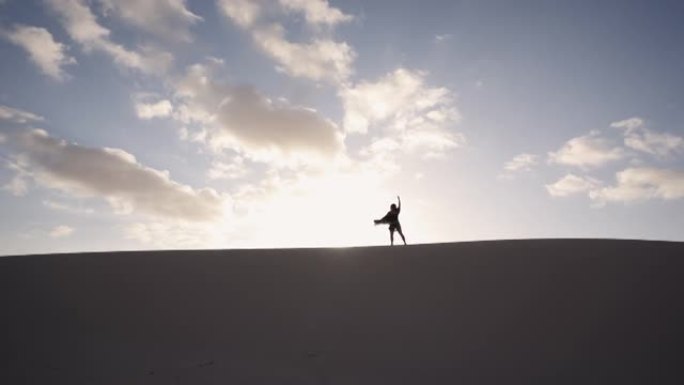 女人在沙丘上跳舞，太阳在后面